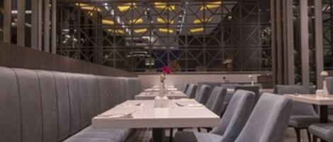 A modern restaurant with a long counter, grey upholstered seating, and recessed ceiling lighting.