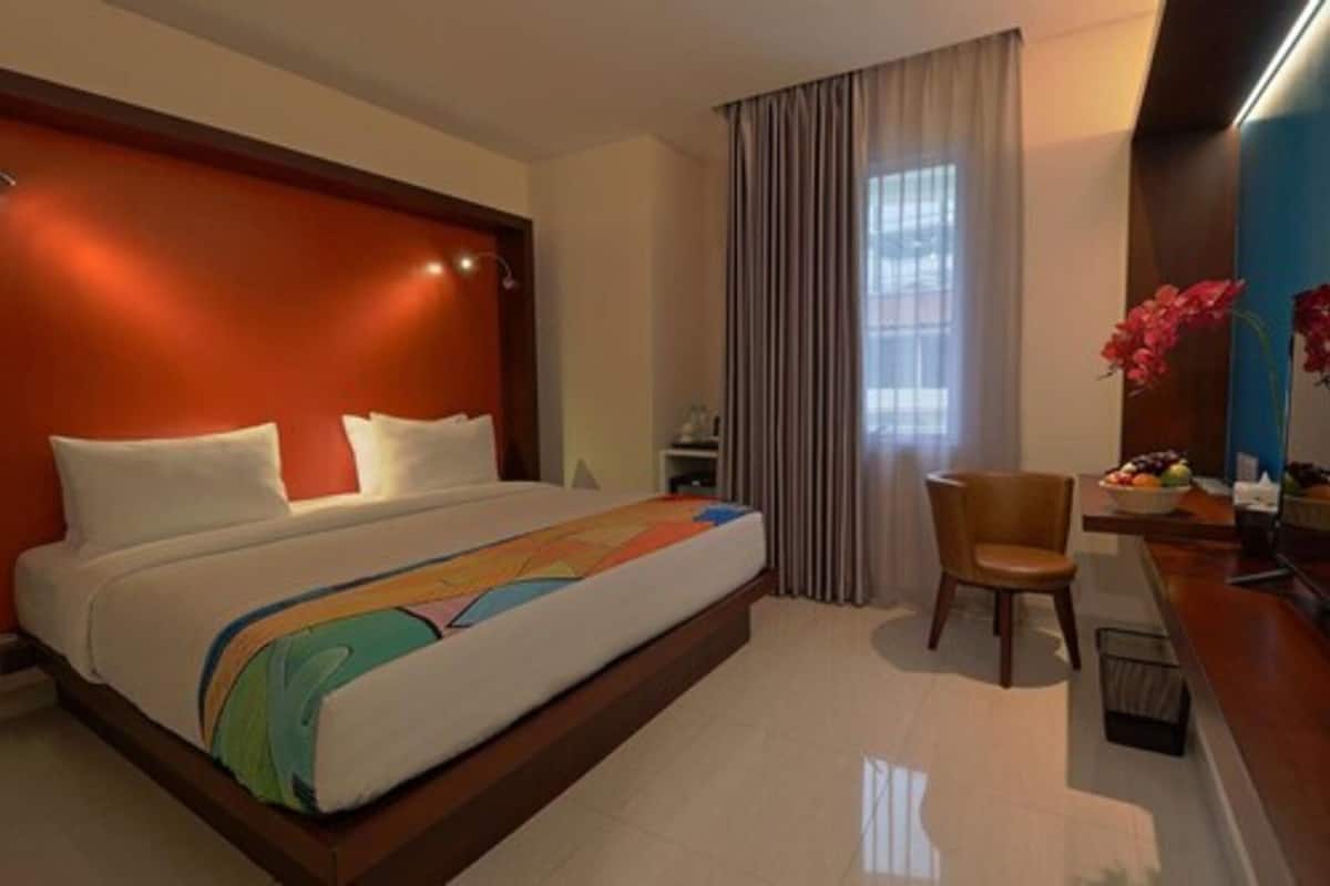Ein Hotelzimmer mit Bett, Stuhl, Schreibtisch und einem Fenster mit Vorhängen.