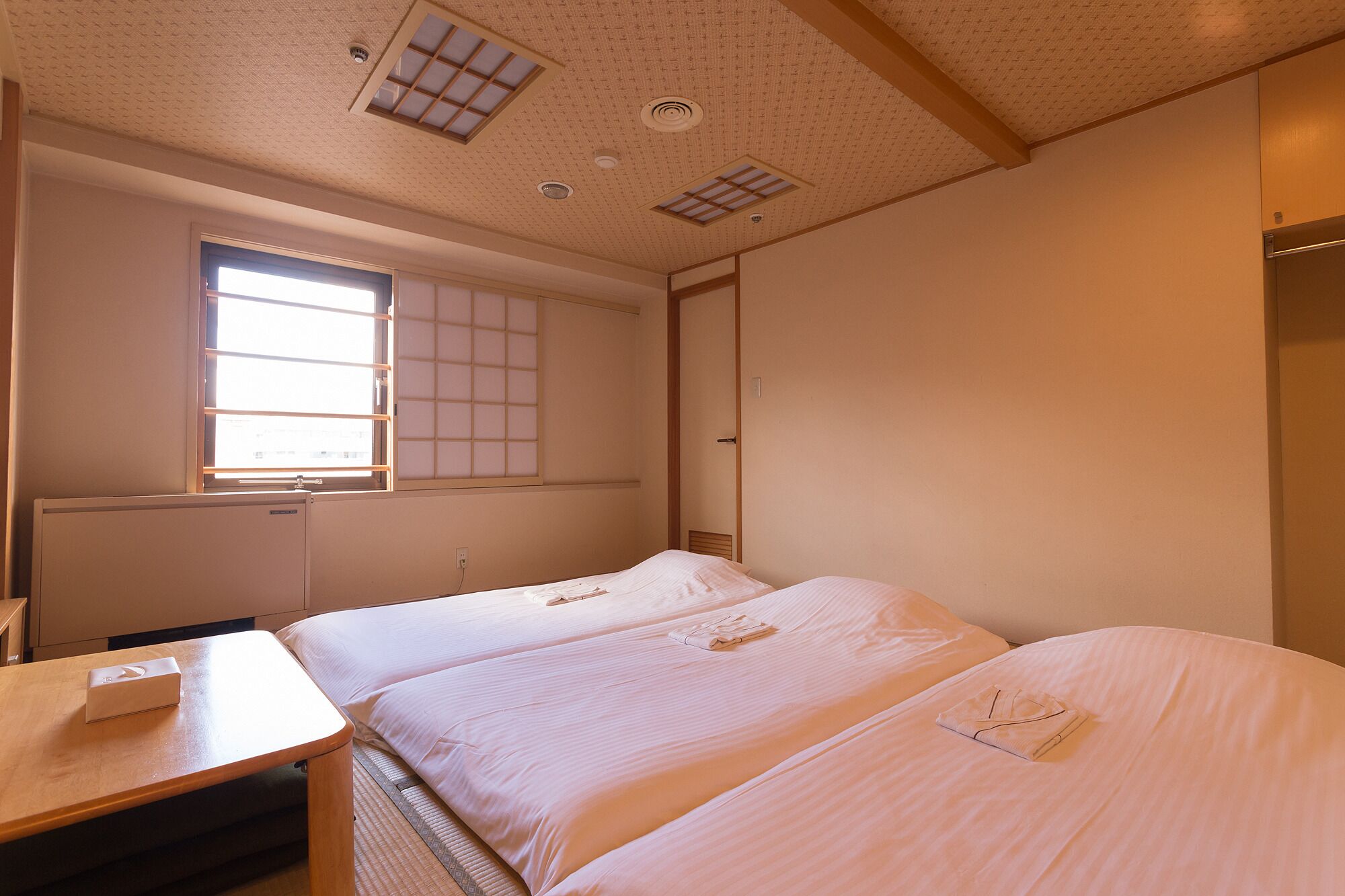 A hotel room with two beds, a desk, and a window with a view.