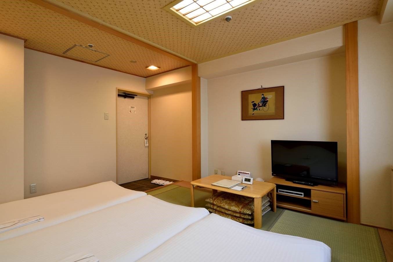 A hotel room with two beds, a television, a small table, and a framed picture on the wall.