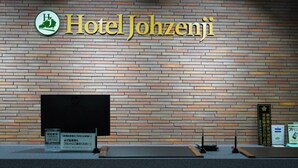 A reception desk at Hotel Johzenji with a brick wall background, a logo, and some informational signs. - Hotel Johzenji (Sendai)
