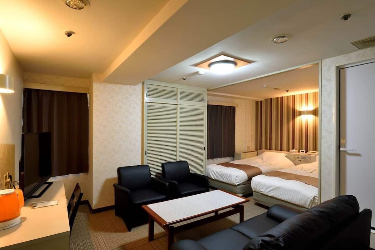 Quarto de hotel com sofá, duas cadeiras, uma mesinha, televisão, cama e guarda-roupa.