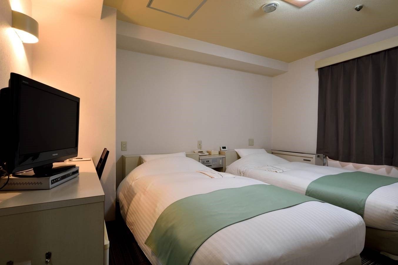 Una camera d'albergo con due letti, una televisione su un mobile, comodini e una tenda.