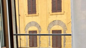 A window view of a yellow building with brown shutters and arched windows. A tray with a bottle, glasses, and food items is placed on a windowsill. - Casa Thiele alla Signoria (Florence)