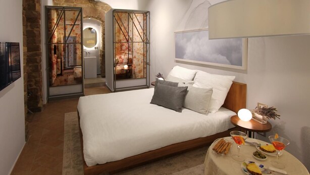 A bedroom with a large bed, a bedside table with a lamp, and a small table with snacks and drinks. - Casa Thiele alla Signoria (Florence)