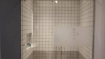 Pequeño baño con azulejos, equipado con un cabezal de ducha y desagüe visible.