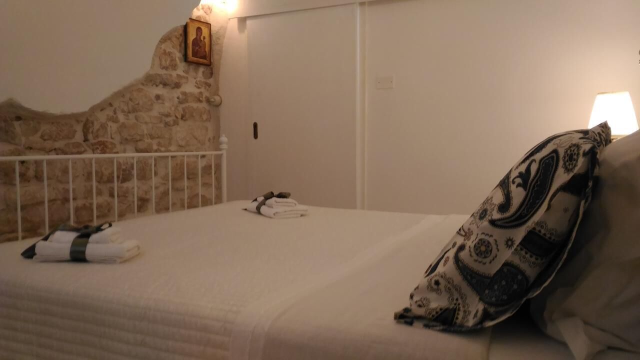 Een bed met een gekleurd kussen, een opgevouwen handdoek en een klein beeldje aan de muur.