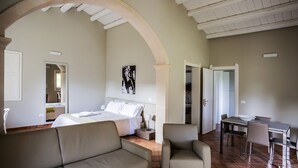 A spacious room with a large bed, a sitting area with a sofa and armchairs, a dining table with chairs, and a view through an arched doorway. - Domus Hyblaea (Palazzolo Acreide)