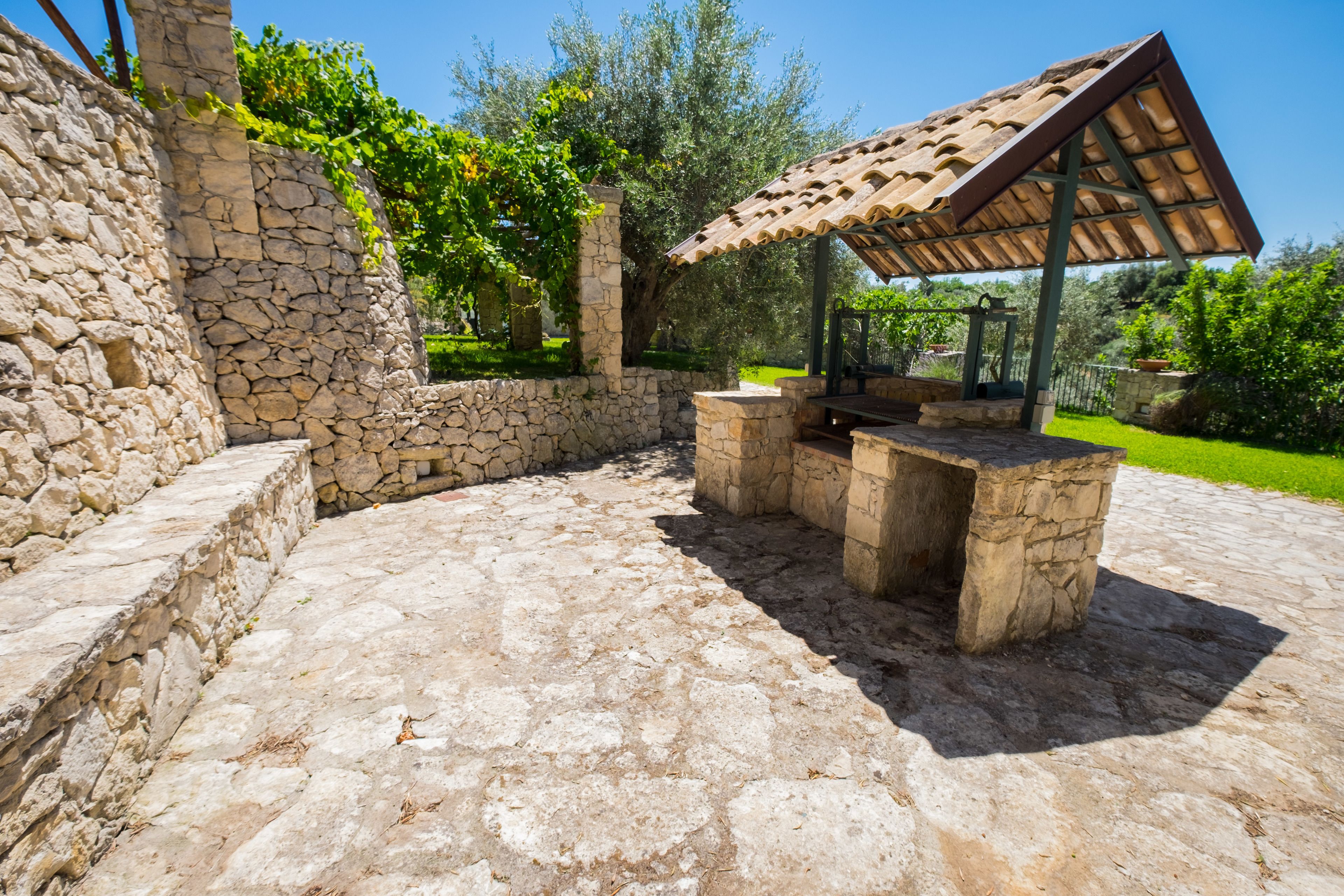 Eine Terrasse im Freien mit Steinboden, einer Pergola mit einem Ziegeldach und einer Steinmauer.