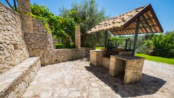 Eine Terrasse im Freien mit Steinboden, einer Pergola mit einem Ziegeldach und einer Steinmauer.