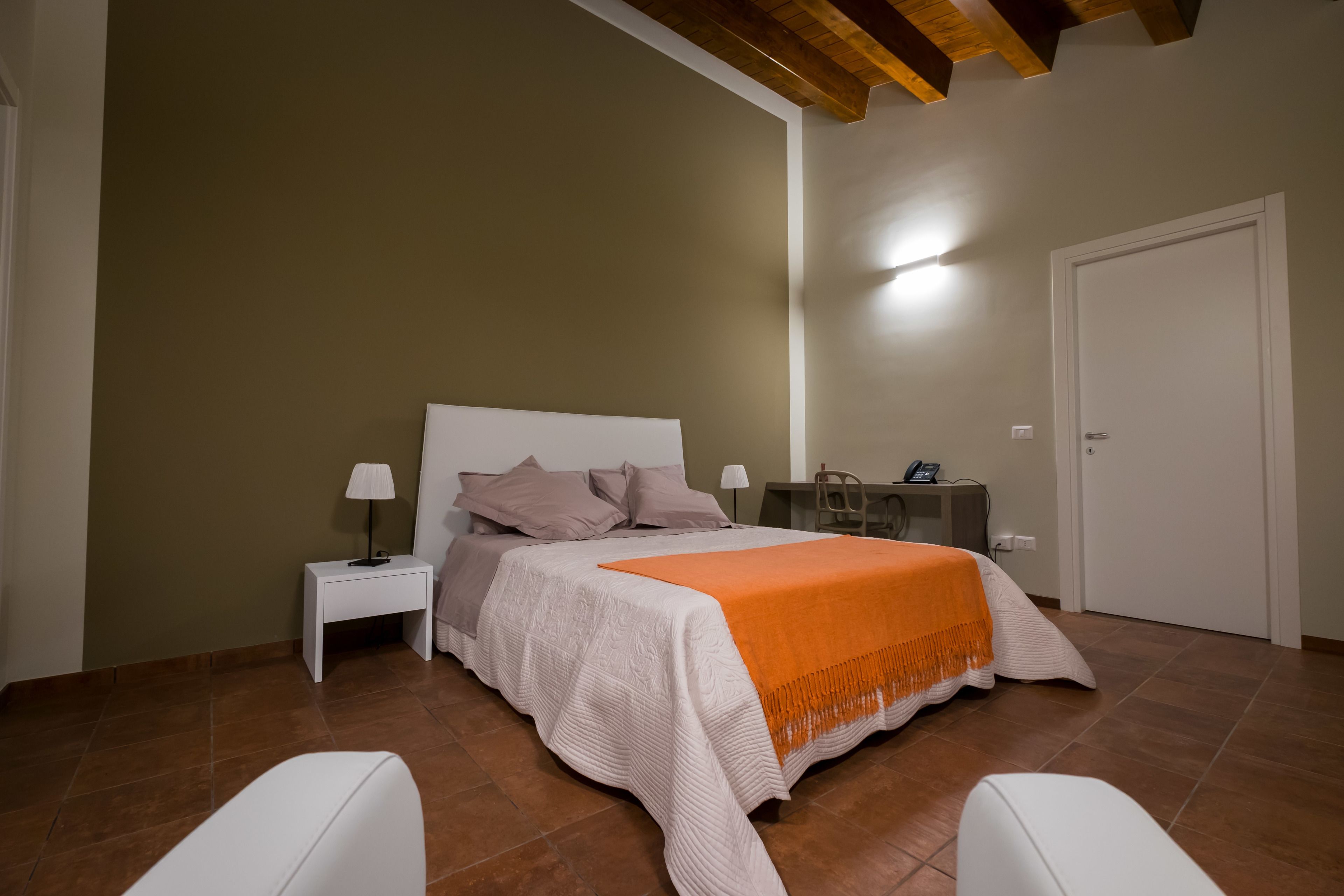 A bedroom with a bed, nightstands, a desk, and a door.