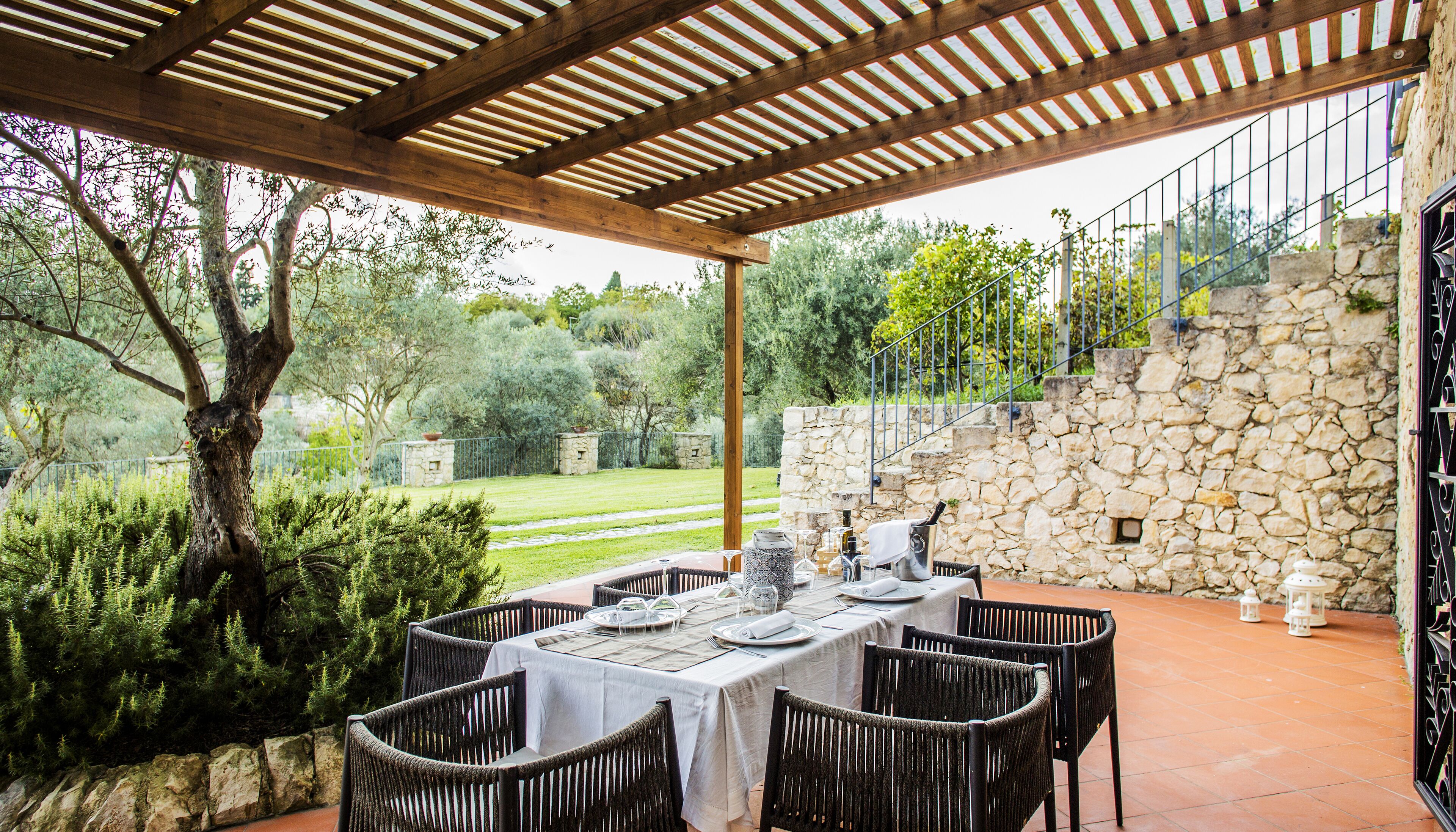 An outdoor patio with a table set for dining, surrounded by stone walls and greenery.