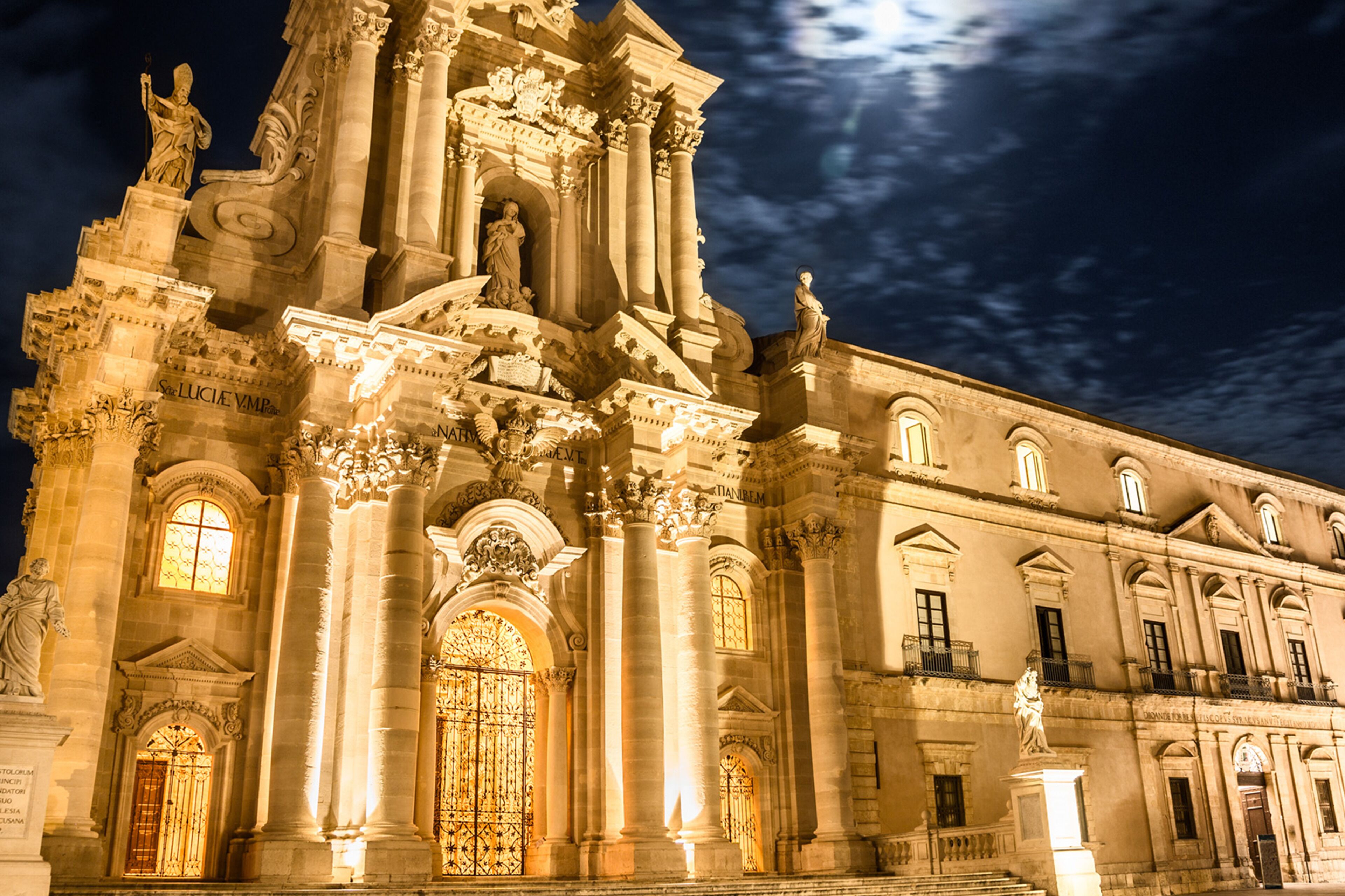 A grand historical building with ornate columns, a large central entrance, and statues.