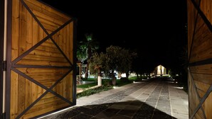 A nighttime view of a pathway leading to a building with wooden doors and stone paving. - Domus Hyblaea (Palazzolo Acreide)