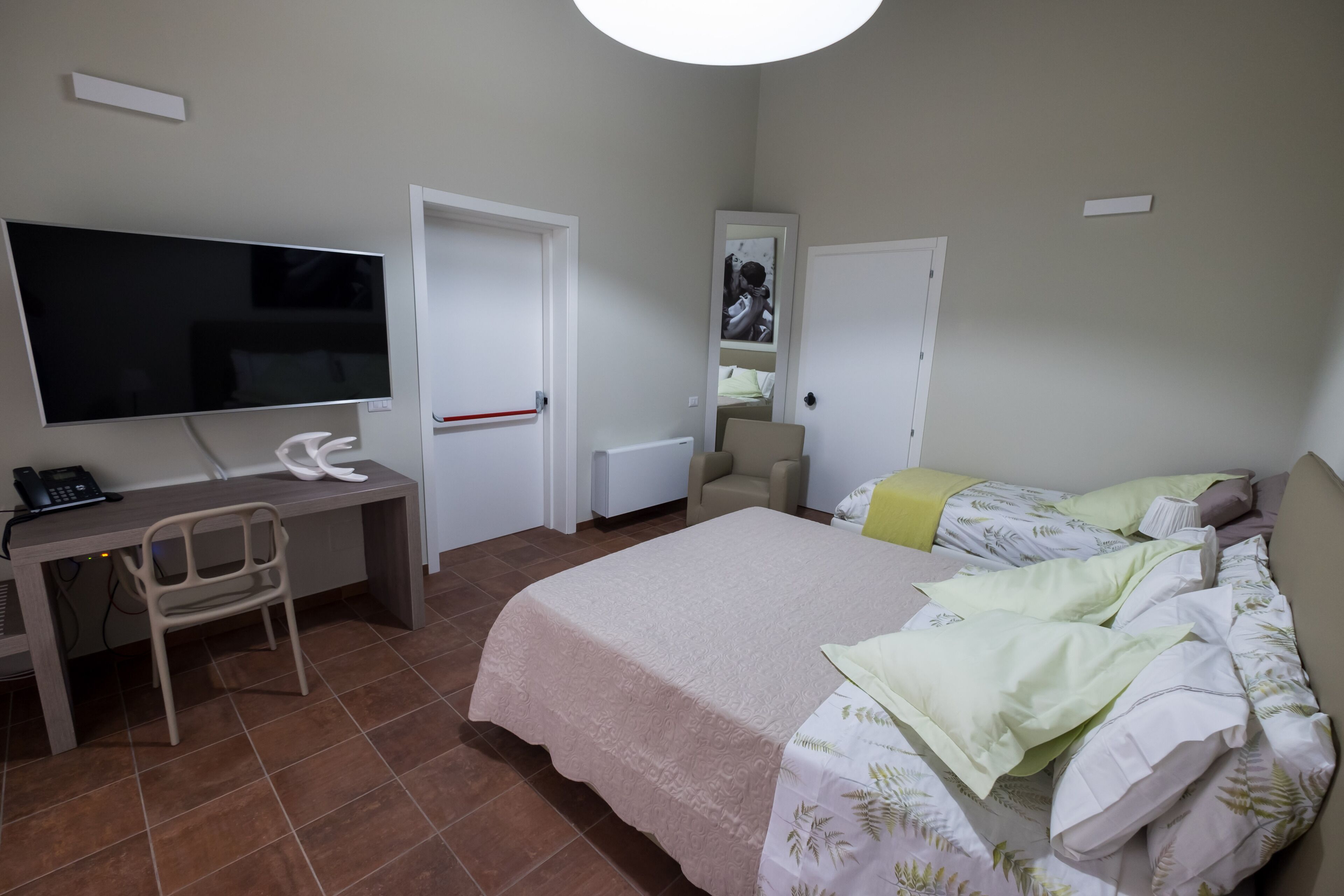Een slaapkamer met een bed, een bureau met stoel, een televisie en een deur naar een badkamer.