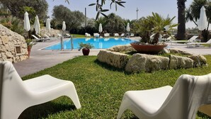 A pool area with lounge chairs, a stone wall, and potted plants. - Domus Hyblaea (Palazzolo Acreide)