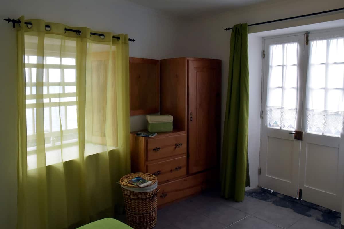 Ein Zimmer mit einem Holzschrank, einem Korbwäschesammler und einem grünen Vorhang.