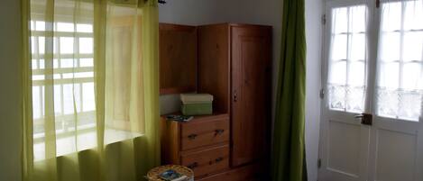 A room with a wooden wardrobe, a wicker basket, and a green curtain.