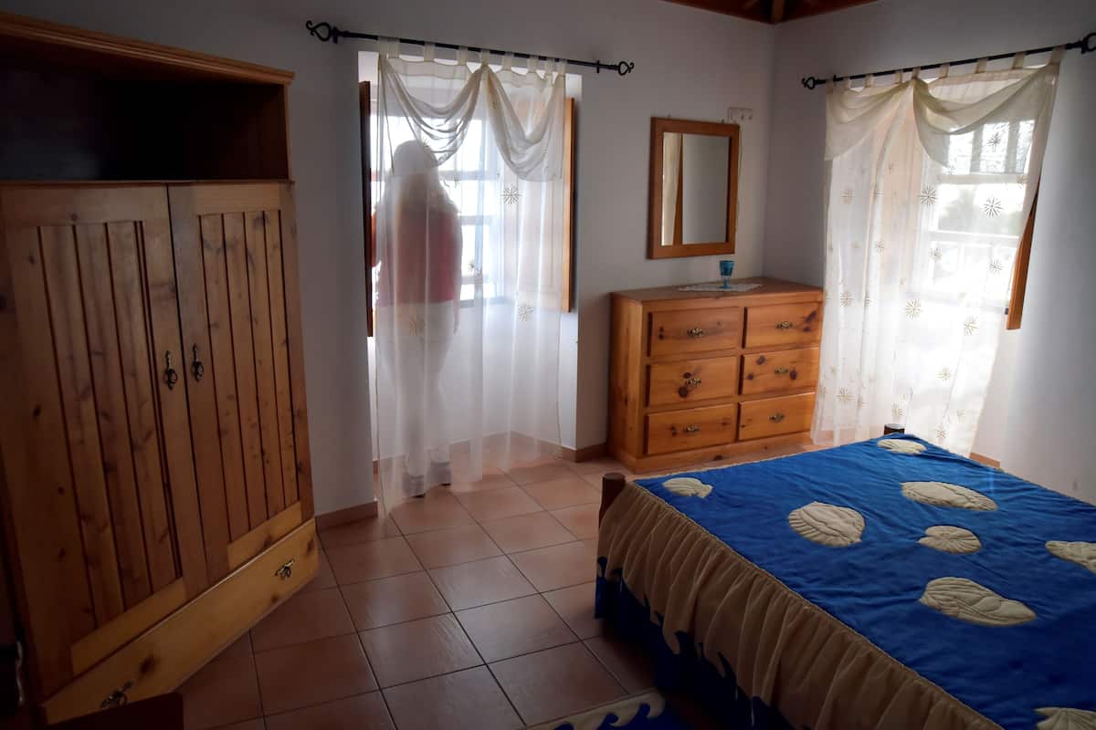 Ein Schlafzimmer mit einem Holzkleiderschrank, einem Bett mit blauer Bettdecke, einer Holzkommode und einem Spiegel an der Wand.