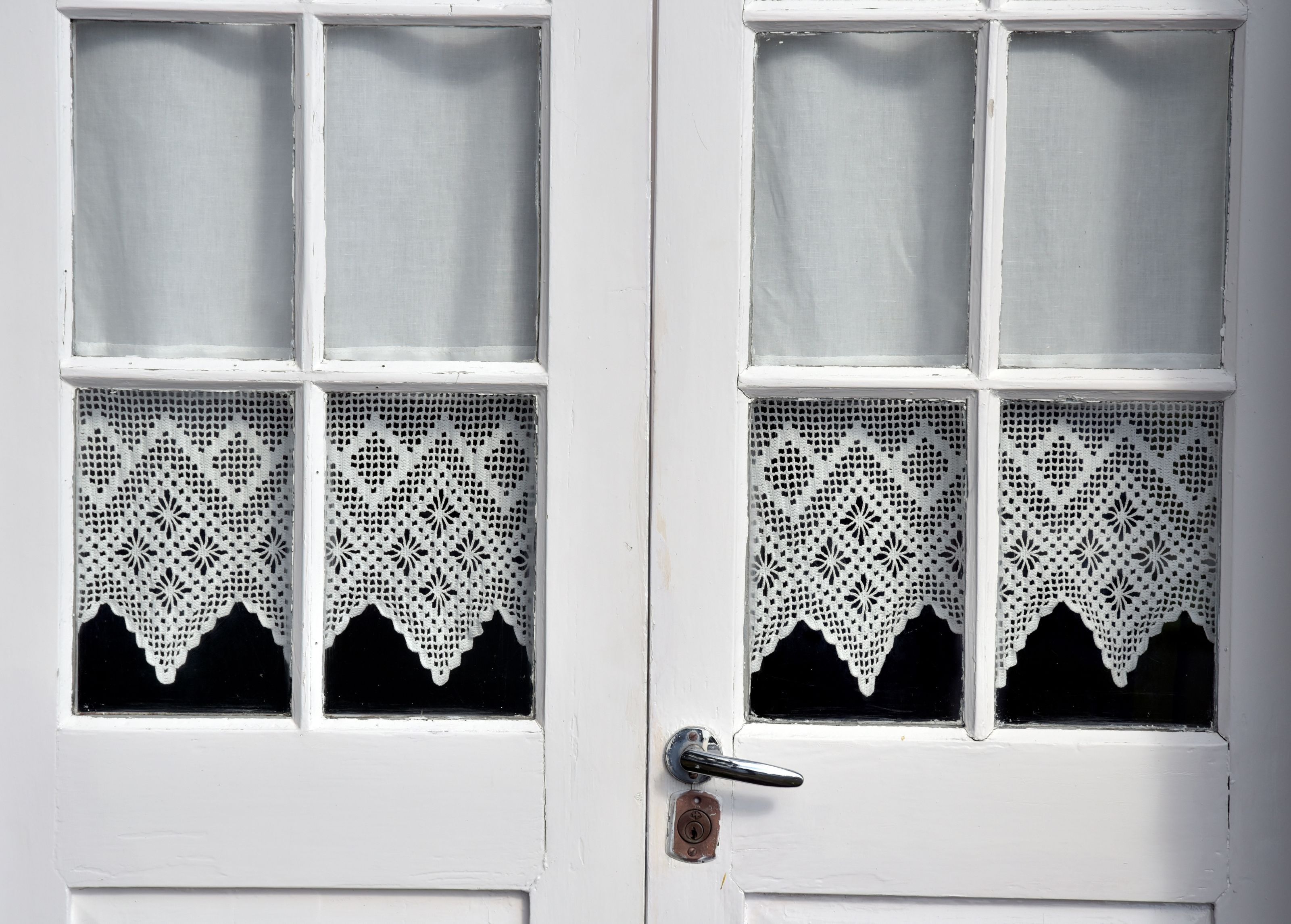 A white door with a keyhole and a handle, featuring a lace window covering and a black lower section.