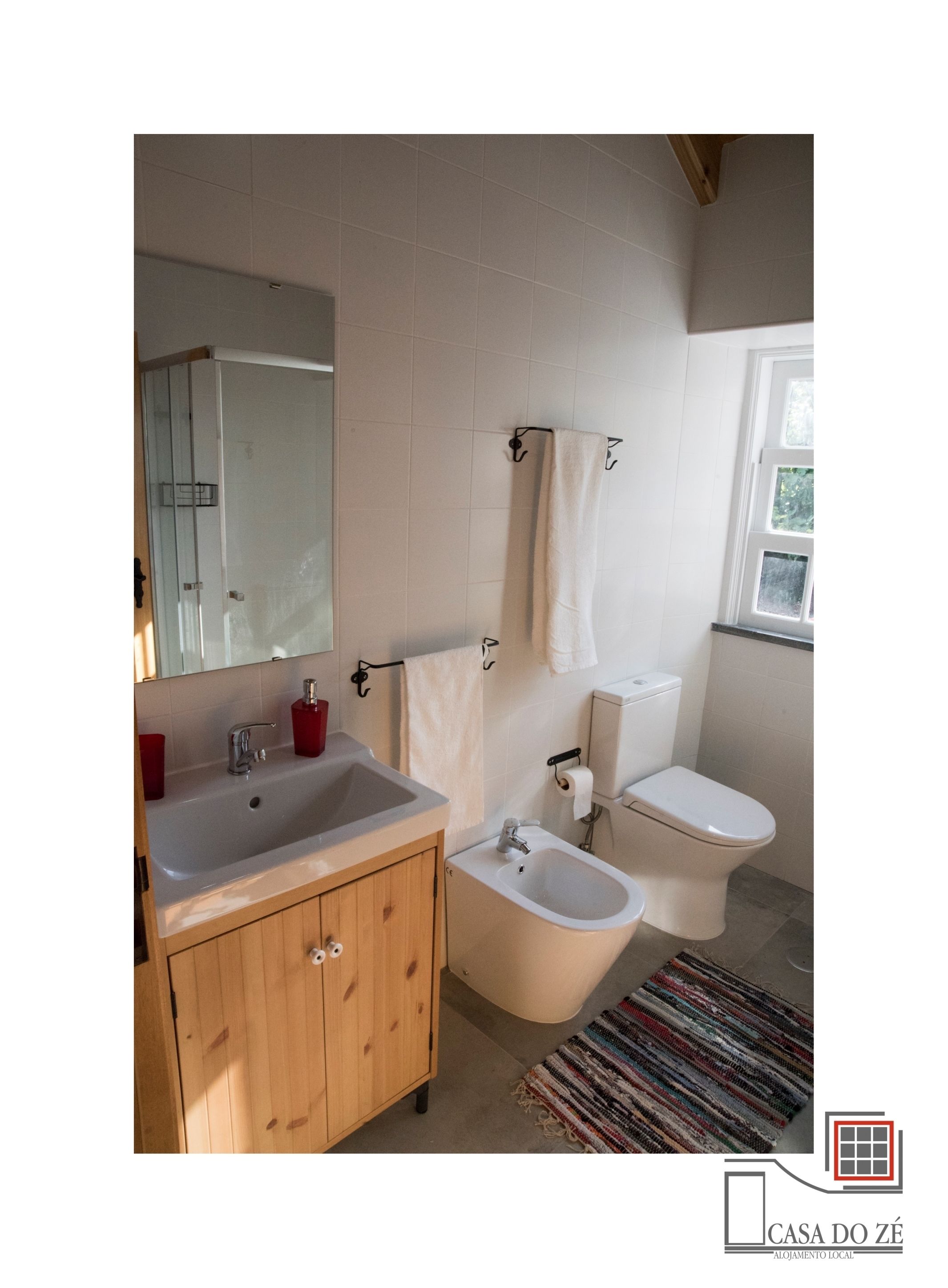 A bathroom with a wooden cabinet, a sink, a bidet, a toilet, and a mirror.