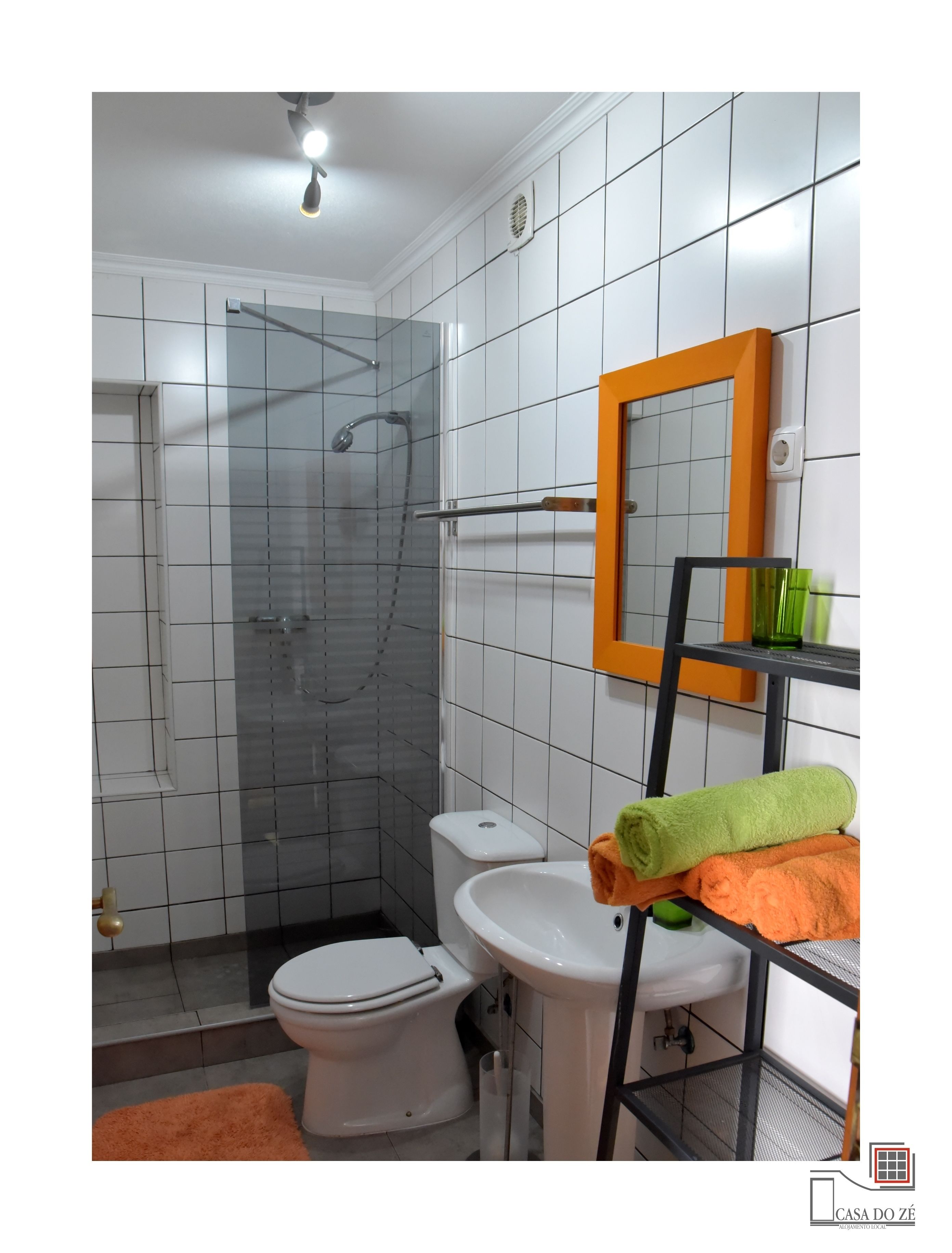 A bathroom with a shower, toilet, sink, and a mirror with a green towel on a rack.