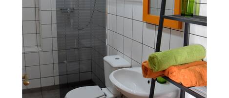 A bathroom with a shower, toilet, sink, and a mirror with a green towel on a rack.