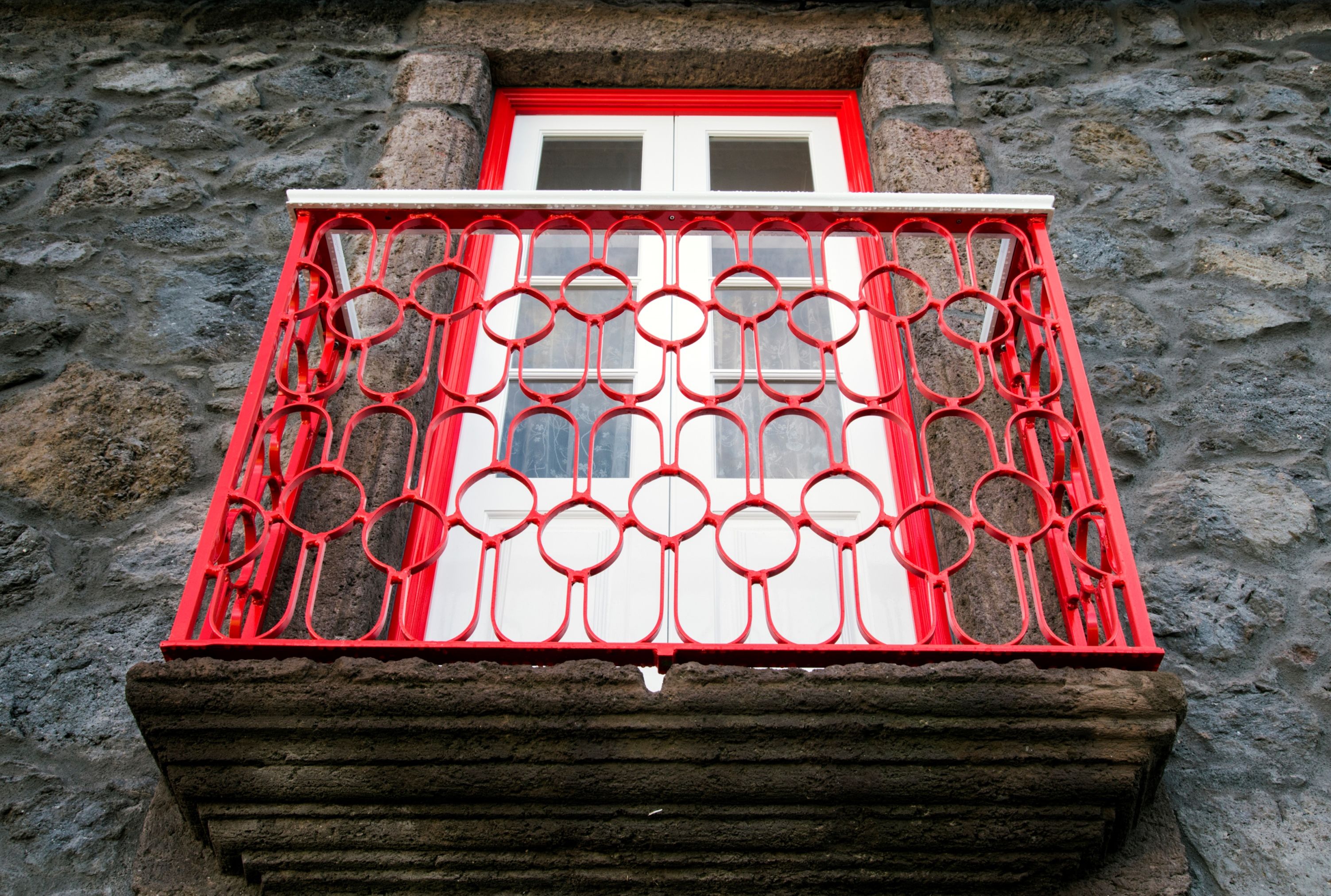 A stone building with a red metal balcony railing and a red door.