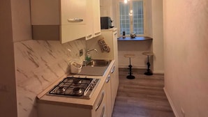 A narrow kitchen with a gas stove, white cabinets, and a wooden ceiling. - Lighthouse Suites Trastevere (Rome)
