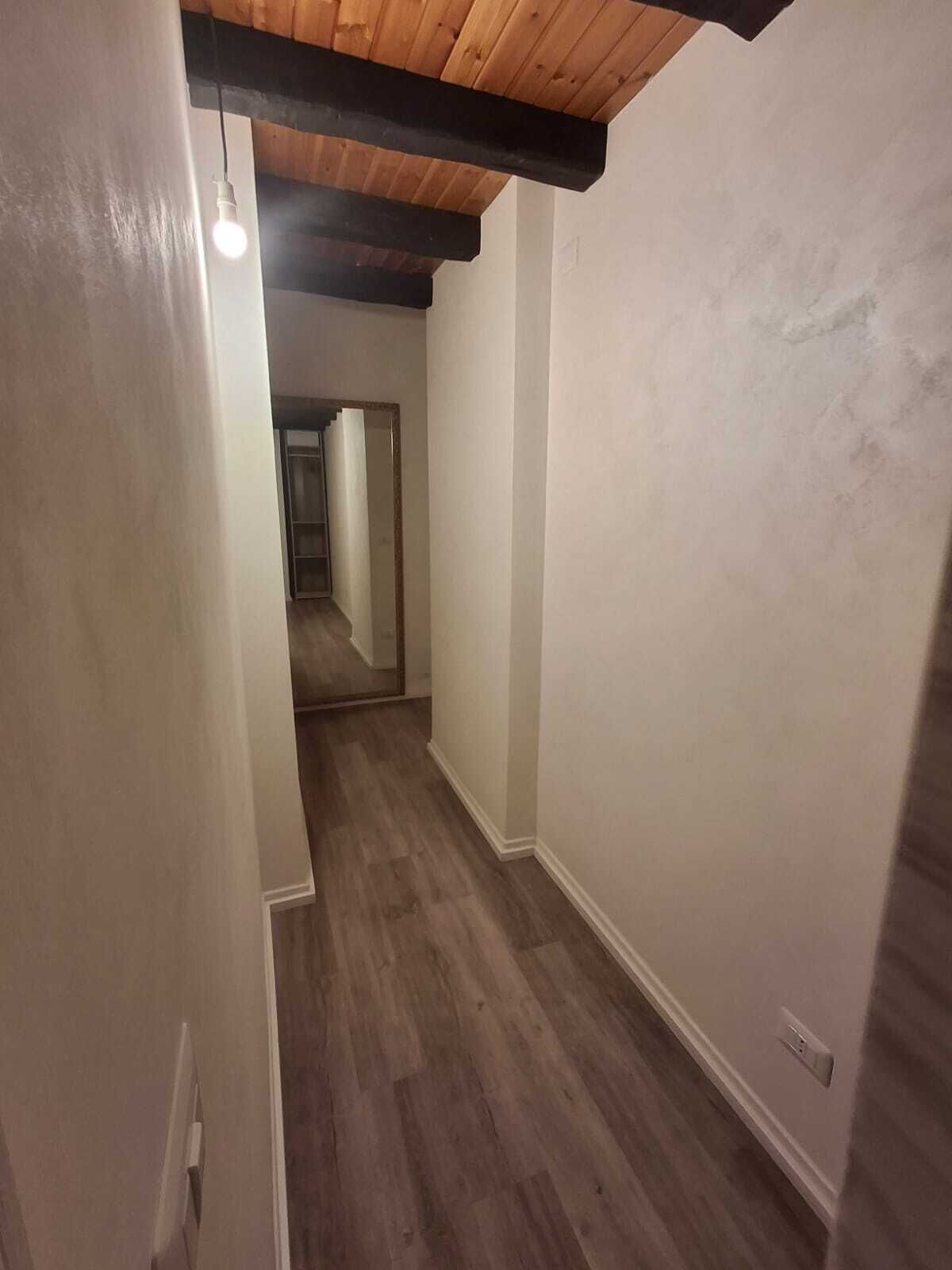 Un pasillo estrecho con suelo de madera y techo inclinado.