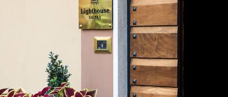 A sign for Lighthouse Suites, a door with a wooden panel design, and a small potted plant.