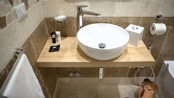 Une salle de bain avec un lavabo blanc, un meuble-lavabo en bois, une serviette, un distributeur de savon et un porte-rouleau de papier toilette.
