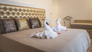 A hotel room with a tufted headboard, a bed with a beige bedspread, and two swan-shaped towels on the bed. - Lighthouse Suites Trastevere (Rome)