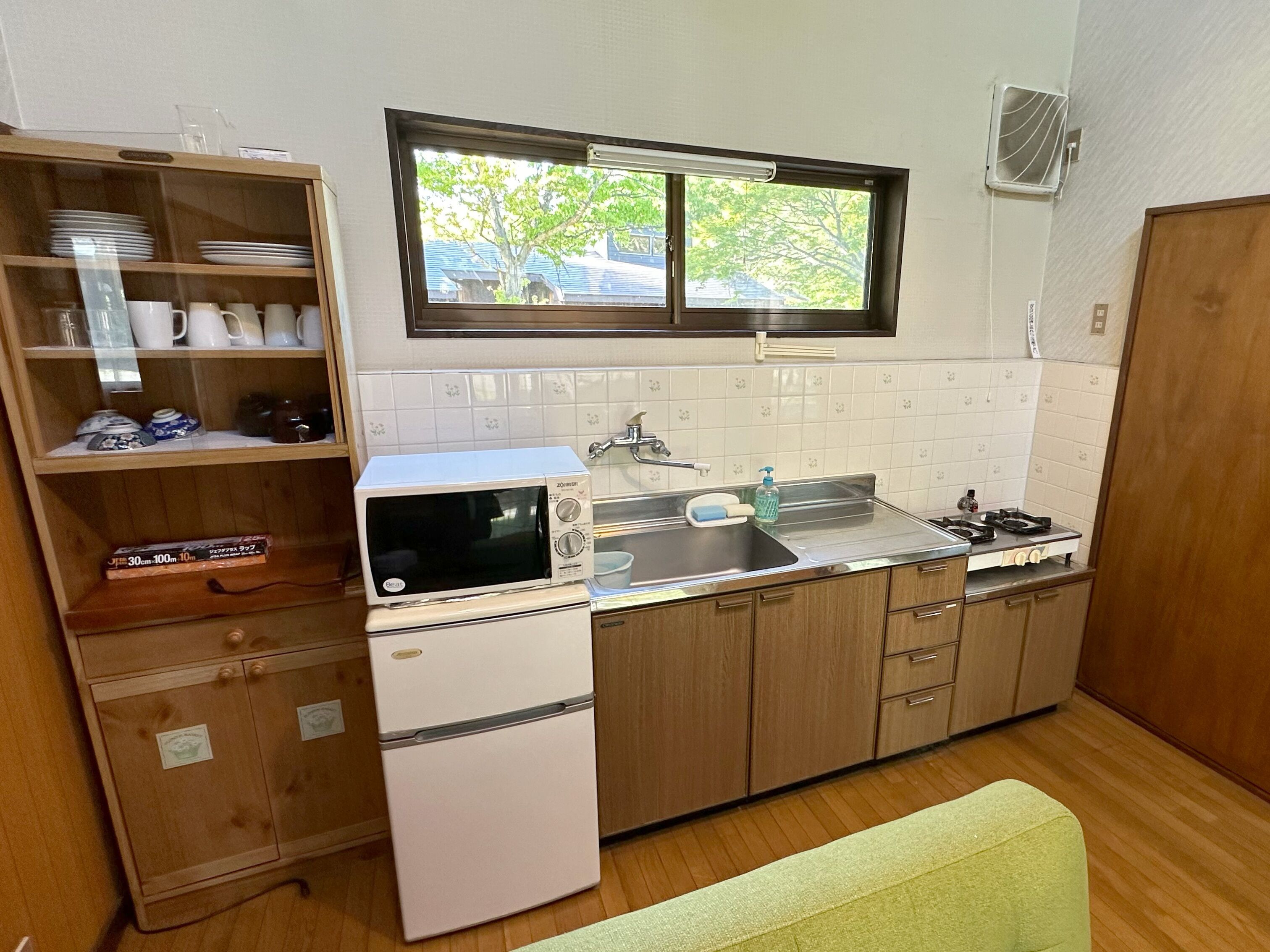 A compact kitchen with a microwave, stove, sink, and a window with a view of trees.