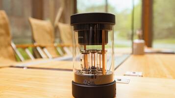 A transparent coffee maker on a wooden table with a window view in the background.