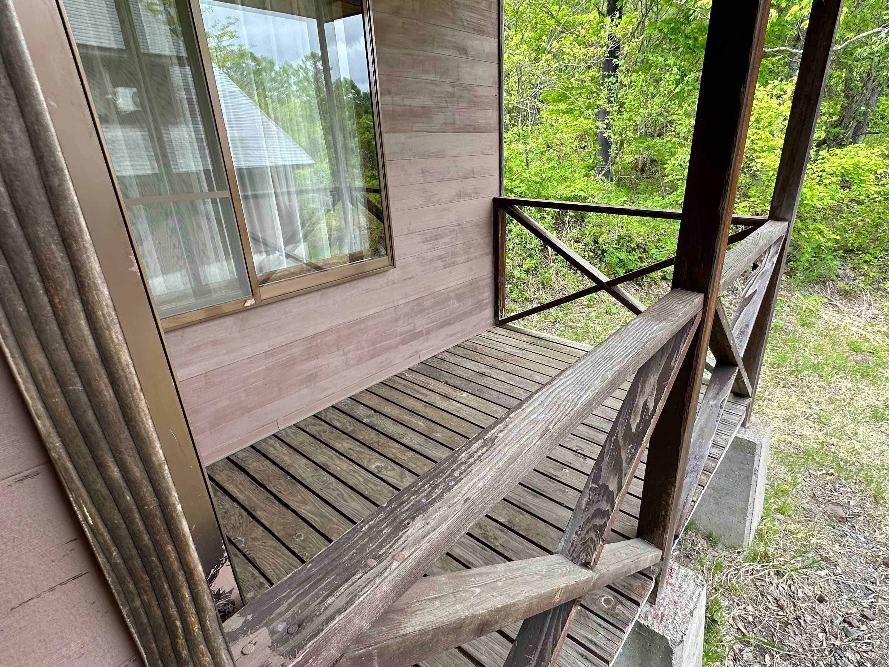 Une terrasse en bois avec une rambarde, une fenêtre et une vue sur la verdure.