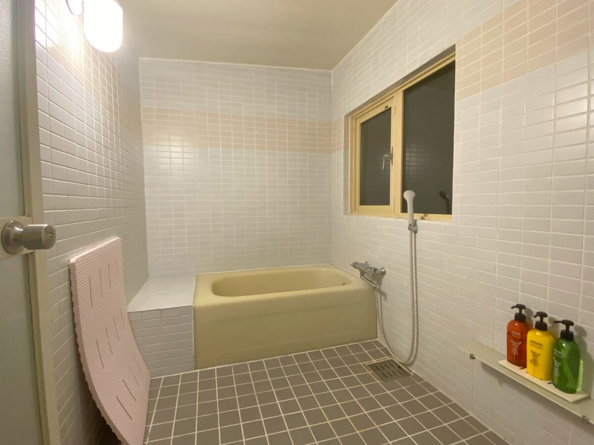 A bathroom with a bathtub, a window, and a shelf with toiletries.