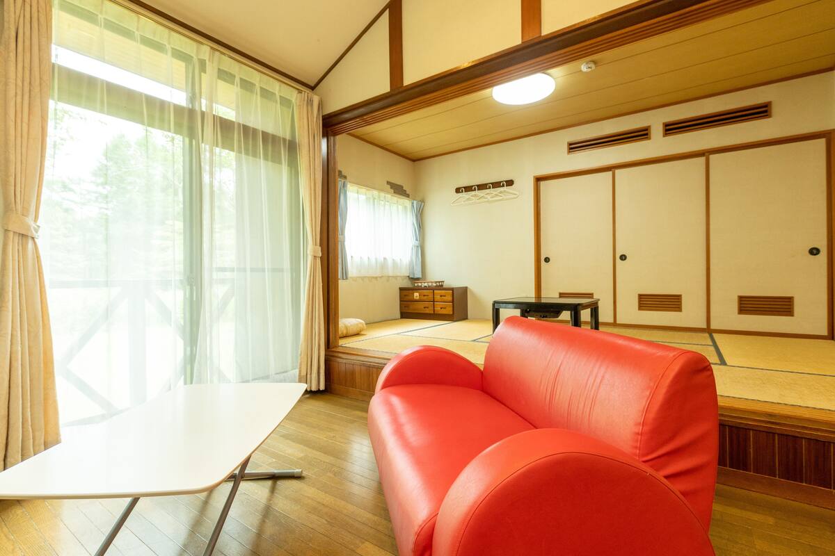 A traditional Japanese room with tatami flooring, a red sofa, a small table, and a sliding door.