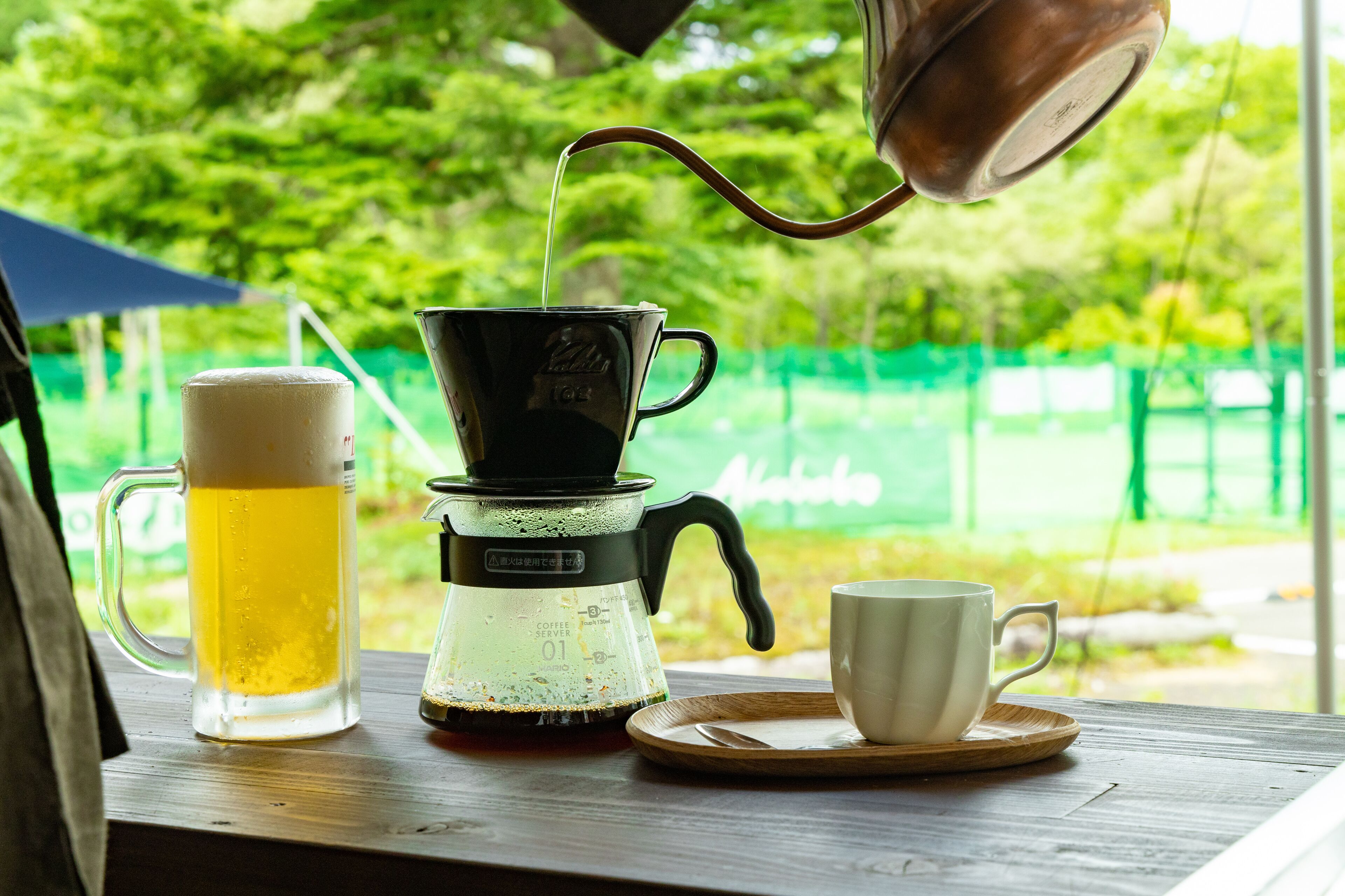 Une machine à café, une tasse et un verre de bière sur une table en bois.