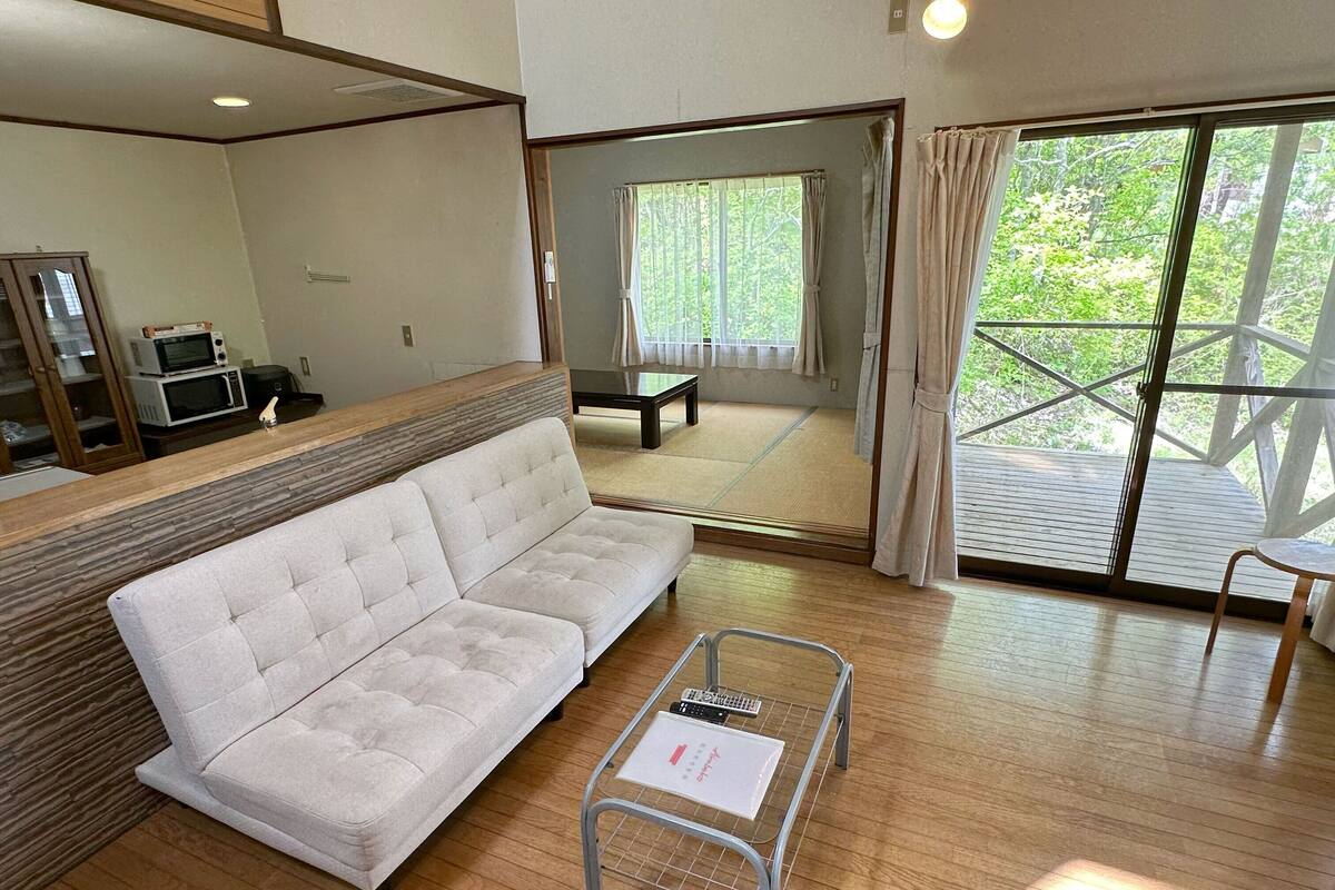 A modern room with a white sofa, a small table with a menu, and a view of a wooden deck and greenery outside.