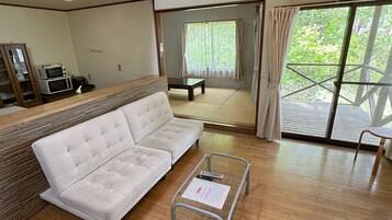 A modern room with a white sofa, a small table with a menu, and a view of a wooden deck and greenery outside.