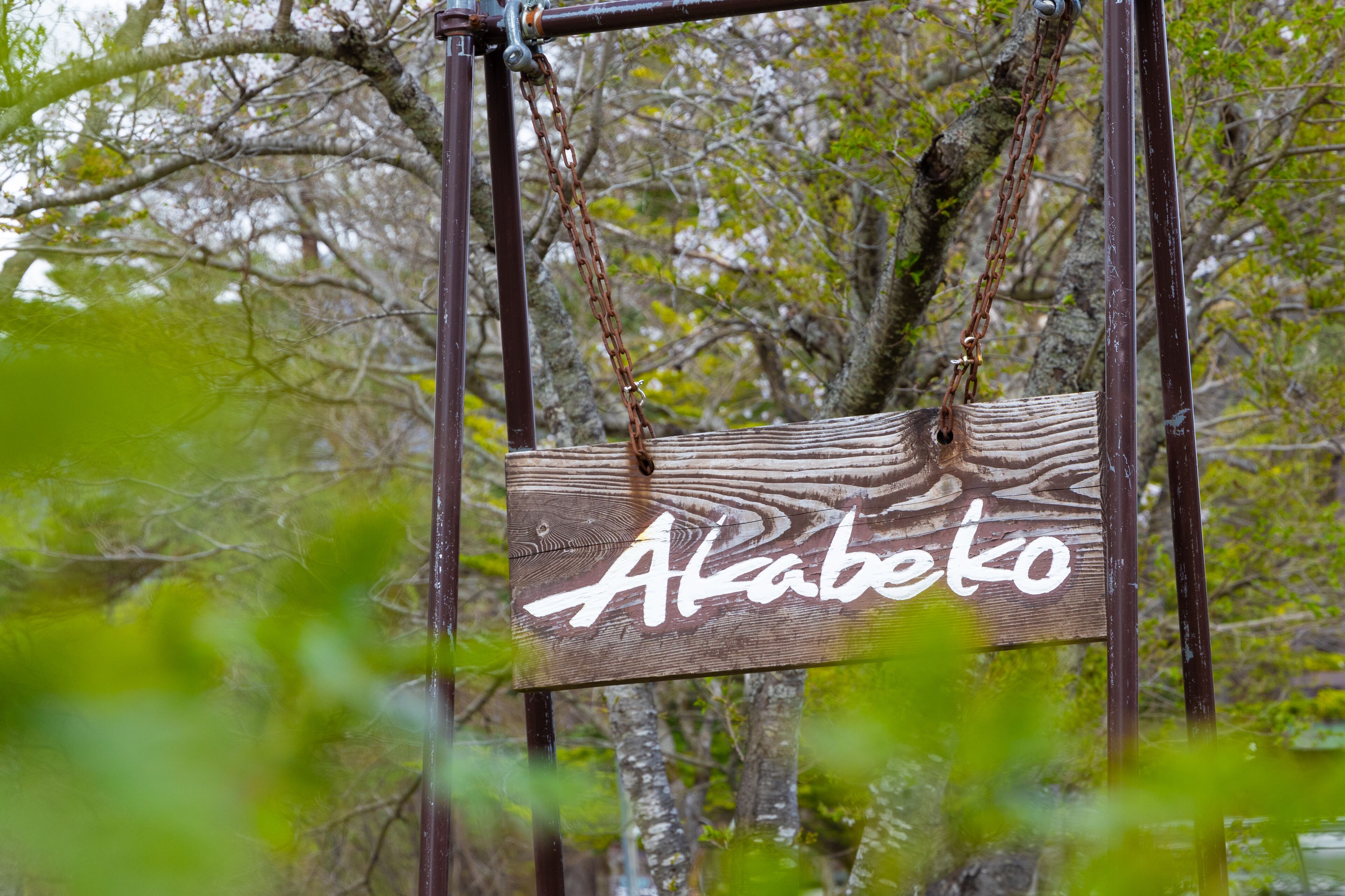 Uma placa de madeira com o nome 'Alabeko' pendurada numa estrutura de metal.