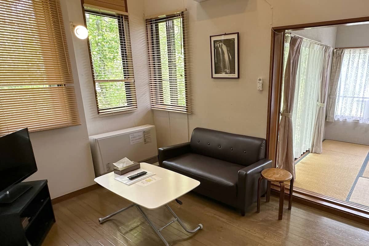 A room with a sofa, a small table, a TV, and a window with blinds.