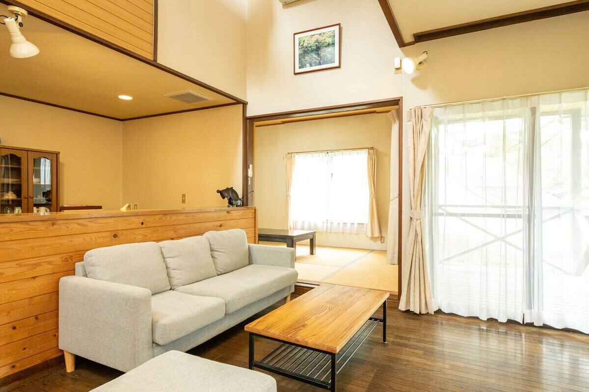 A room with a sofa, a wooden coffee table, a wooden bench, and a large window with curtains.