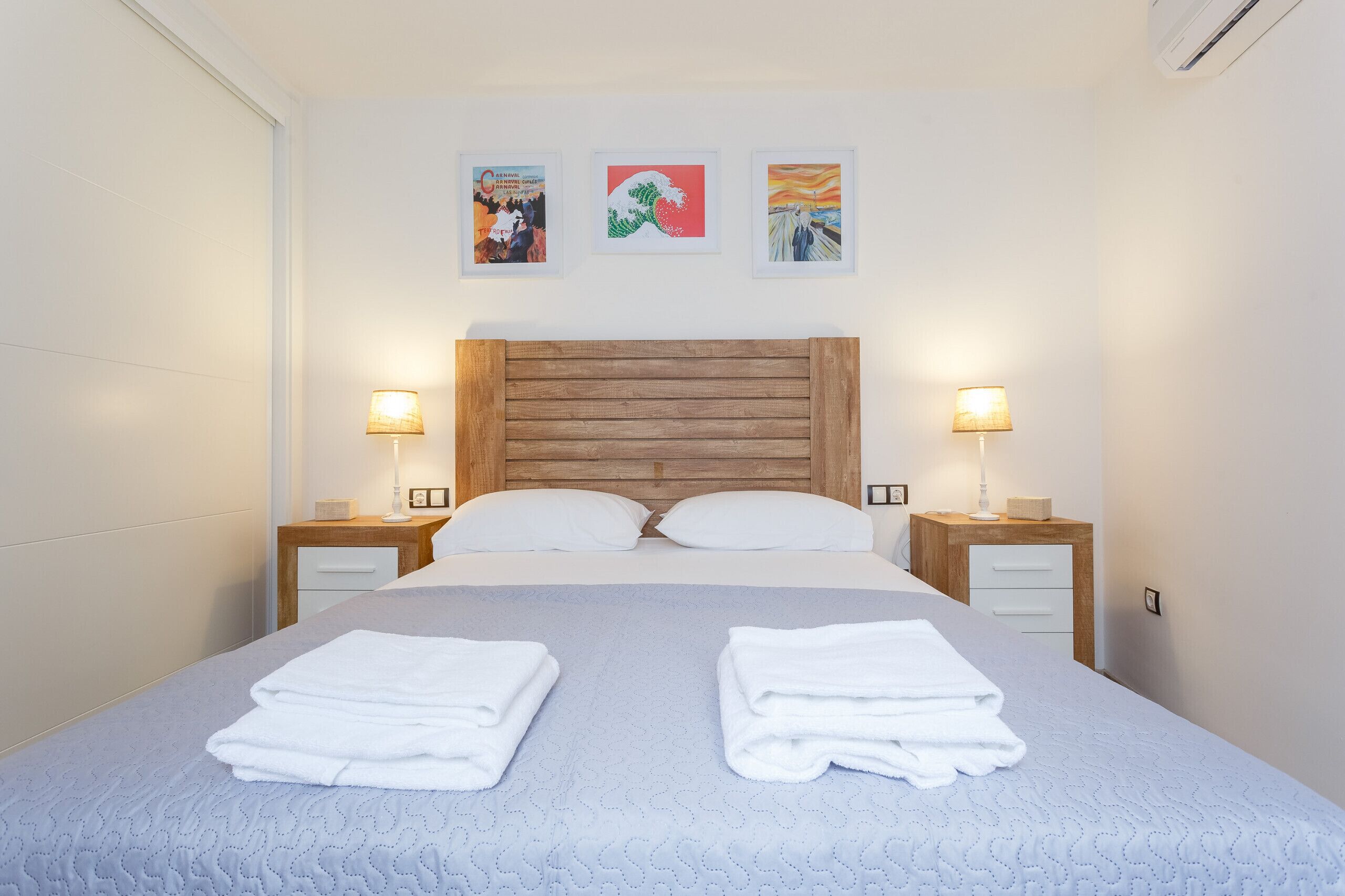 Ein ordentlich bezogenes Bett mit zwei Kissen, zwei Nachttischen mit Lampen und drei gerahmten Kunstwerken an der Wand.