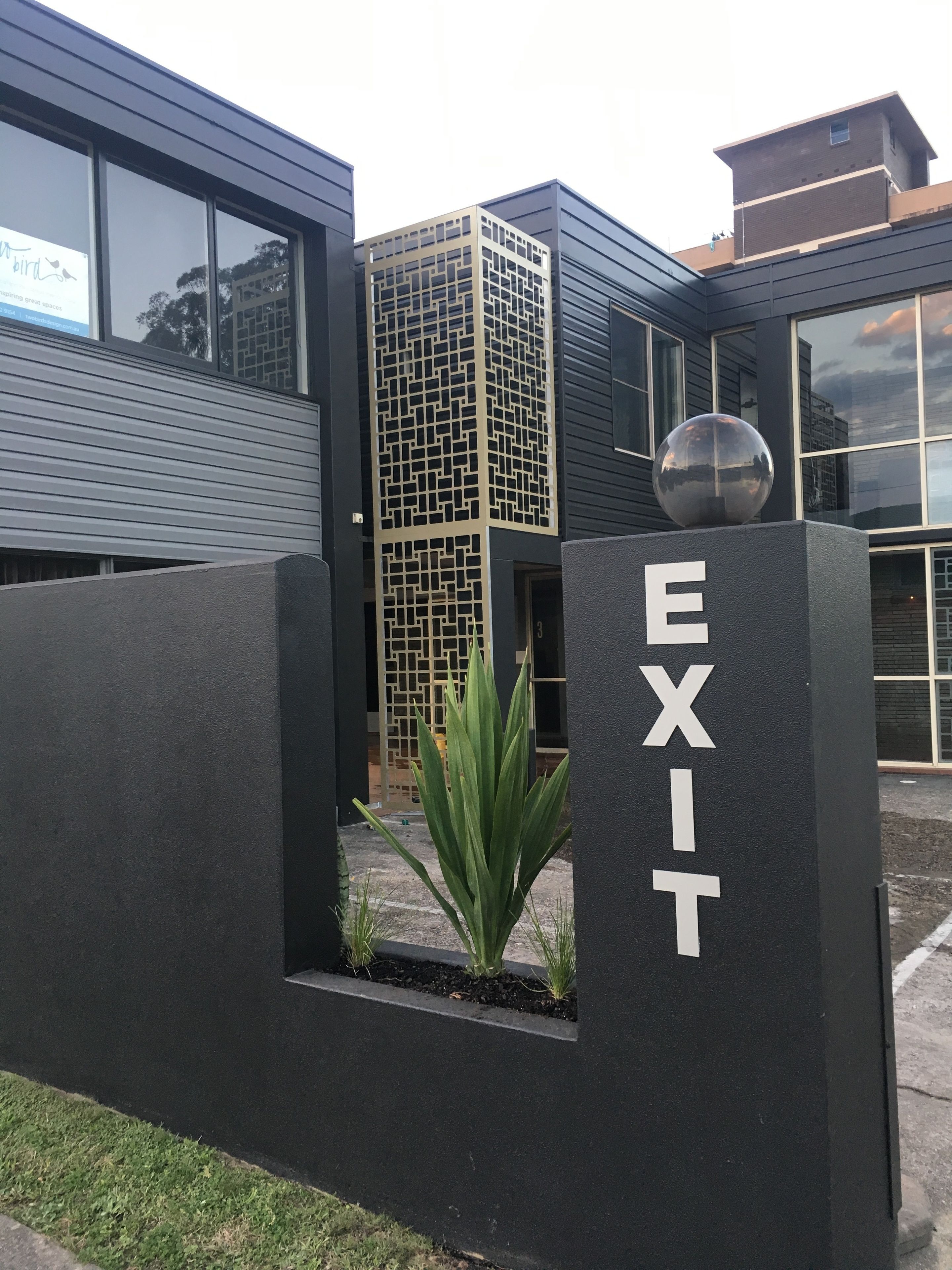 Ein modernes Gebäude mit einem gut sichtbaren 'EXIT'-Schild, einem sphärischen Dekorationselement und einer vertikalen Glasfassade.