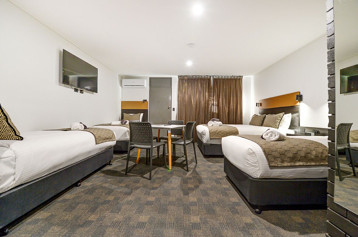 A hotel room with two single beds, a small table, two chairs, a TV, and a window with curtains.