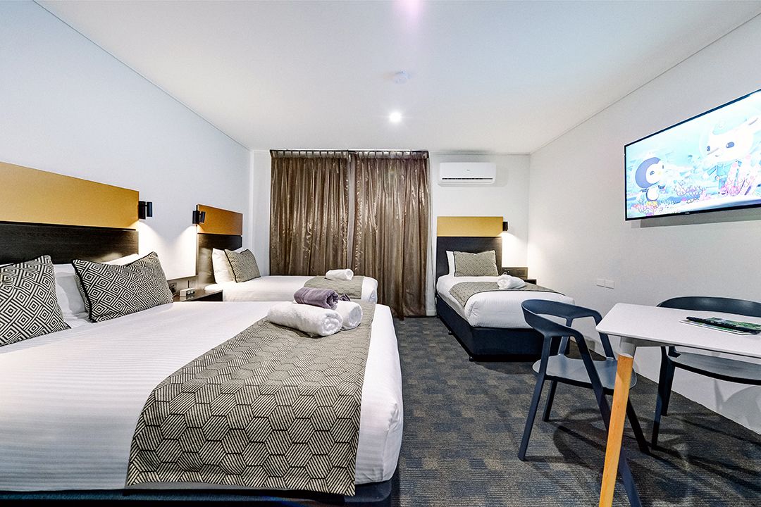 A hotel room with two beds, a desk, and a TV.