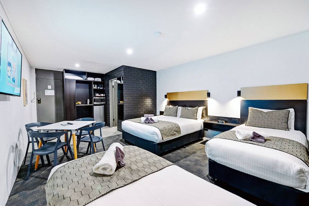A hotel room with two beds, a dining table, and a kitchenette.