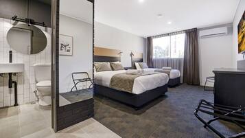 A modern hotel room with a large bed, a separate bed, a bathroom with a toilet and sink, a mirror, and a window with curtains.